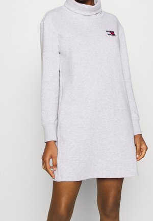 Robe-pull gris clair à manches longues avec col montant drapé et petit logo Tommy Hilfiger sur la poitrine, portée par une personne à la peau foncée.