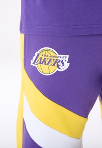 Lila rövidnadrág sárga és fehér átlós csíkokkal, bal oldalán "Los Angeles Lakers" logóval és kosárlabda grafikával.