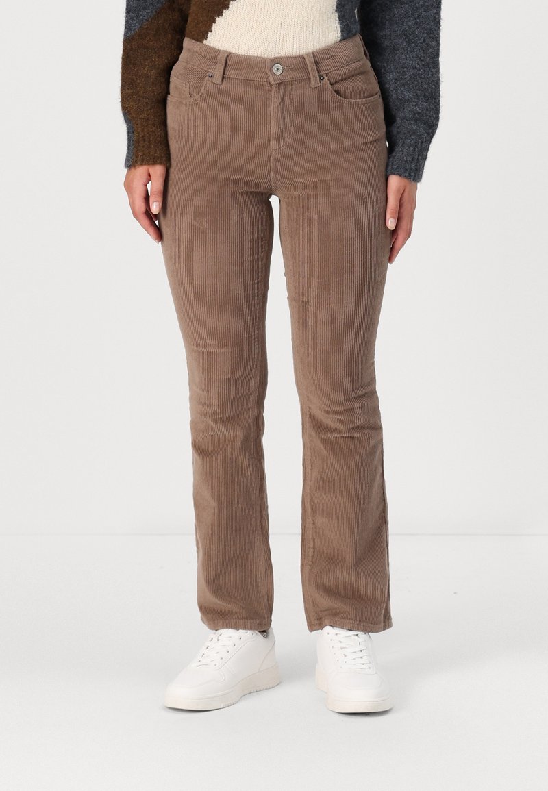 Pantalon en velours côtelé marron coupe droite, porté avec des baskets blanches et un pull en maille multicolore.