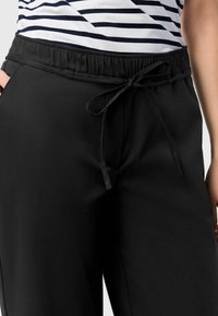 Black elastic waistband pants with a tie closure, featuring a smooth texture and side pockets. The top partially shows striped design.
