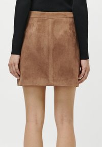 Fustă mini din suede maro cu linii curate și o textură netedă, având un design simplu și o finisare la margine degajată.