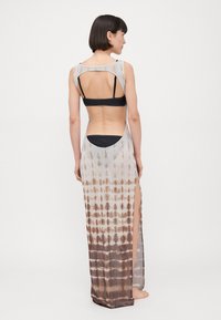 Long, sheer cover-up dress in gradient tie-dye pattern, featuring open back design, high slits, and black undergarment visible.