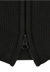 Primo piano di tessuto a maglia nero a coste con una zip di plastica nera parzialmente aperta al centro.