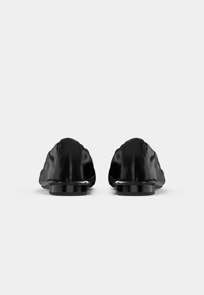 Une paire de mocassins en cuir noir brillant vus de l'arrière sur un fond blanc uni.