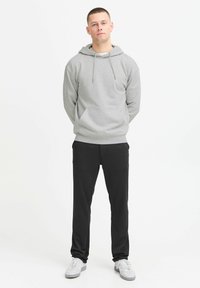 Grå hettegenser med snor, frontlomme, kombinert med svarte tapered bukser og hvite joggesko. Enkel design.