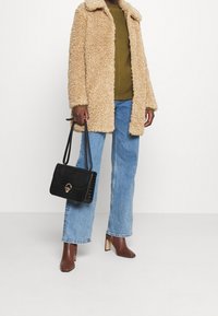 Cappotto in pelliccia sintetica beige, top verde oliva, jeans a gamba larga azzurri chiari, stivaletti con tacco marroni e borsa nera in pelle effetto coccodrillo.