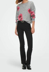 Grauer Pullover mit pinken Blumenmustern, schwarze enganliegende Jeans und schwarze Knöchelstiefel. Der Pullover hat einen lockeren Schnitt und einen runden Ausschnitt.