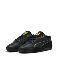 Zapatillas de cuero y ante negro con un diseño elegante, que cuentan con una superficie texturizada, cordones, un logo amarillo y acentos blancos en los laterales.