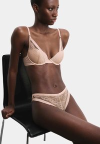 Conjunto de lencería de encaje en color nude que incluye un sujetador triangular con tirantes ajustables y unas braguitas semitransparentes a juego que exhiben patrones intrincados.