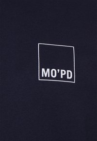 Tissu sombre avec un carré délimité en blanc contenant le texte "MO'PD" en lettres majuscules grasses.