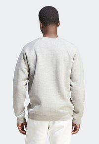 Šedá mikina s texturovaným fleecovým materiálem, raglánovými rukávy a kulatým výstřihem, nošená s bílými kalhotami. Minimalistický design, bez vzorů.