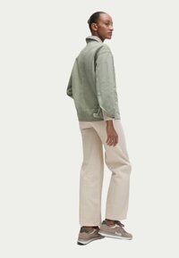 Giacca verde chiaro con una texture morbida, pantaloni a gamba larga crema e sneakers marroni con accenti verdi, mostrati di lato.