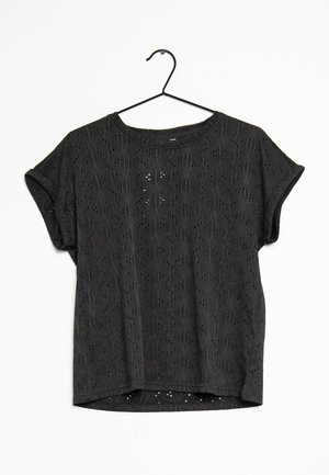 Black short-sleeve blouse with embroidered floral eyelet pattern, loose fit, rounded neckline, hanging on a black metal hanger.