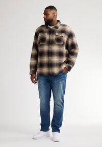 Camicia in flanella a quadri beige e blu navy, con due tasche sul petto e bottoni. Abbinata a jeans azzurri chiari e sneakers bianche.