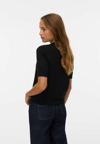 Pull noir à manches courtes au design ajusté, avec un col et un ourlet côtelés, associé à un jean taille haute bleu foncé. Texture lisse.