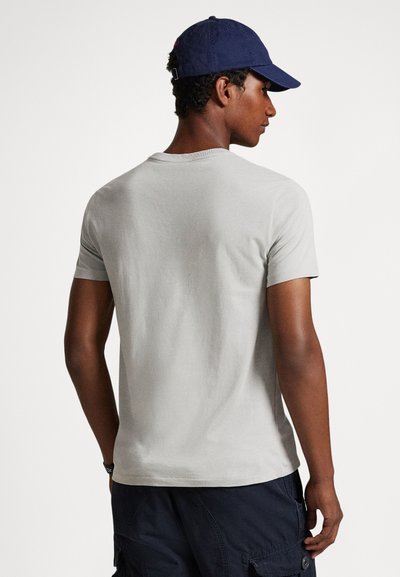 Γκρι κοντομάνικη μπλούζα με στρογγυλή λαιμόκοψη, ομαλή υφή και μίνιμαλ σχεδιασμό, συνδυασμένη με σκούρο μπλε καπέλο και σκούρα cargo σορτς.