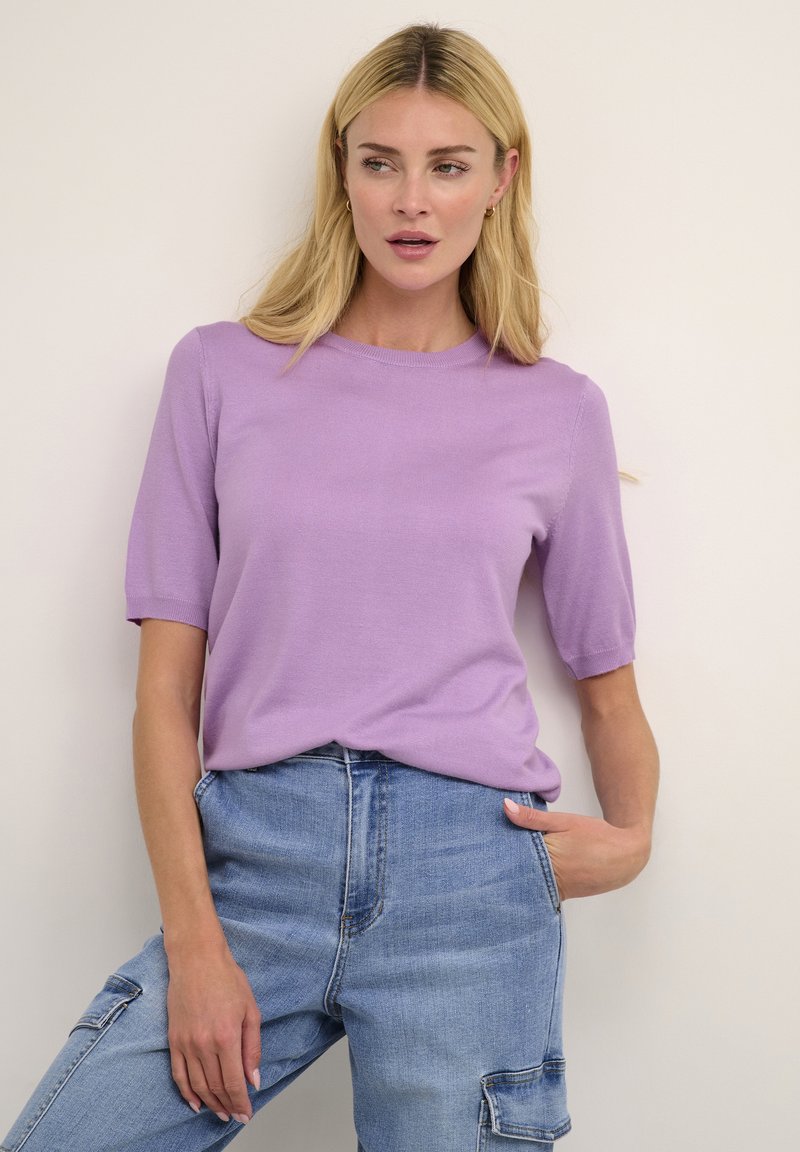 Top corto a maniche corte di colore viola chiaro con scollatura rotonda, realizzato in un tessuto morbido; indossato con jeans in denim blu a vita alta con tasche.