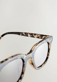 Ochelari de soare cu model țestoasă, cu ramă de un albastru deschis, având o finisare lucioasă și margini rotunjite. Accente de metal argintiu vizibile pe pârghii.