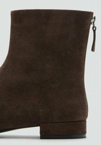 Brązowy zamszowy botek za kostkę o gładkiej fakturze, zaokrąglonym kształcie, niskim obcasie oraz bocznym zamku błyskawicznym ułatwiającym zakładanie.