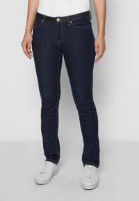Mørkeblå jeans laget av denim, med slim fit, gyldne detaljer og subtile sømmer. Kombinert med hvite joggesko.