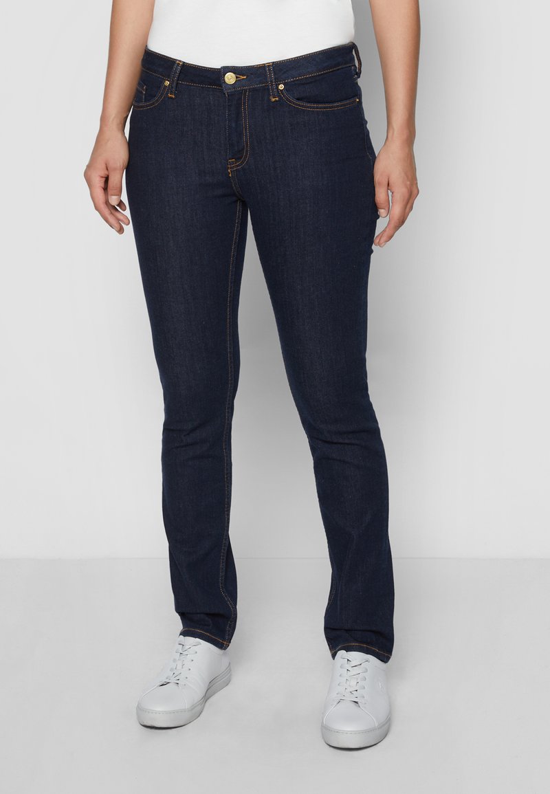 Mørkeblå jeans laget av denim, med slim fit, gyldne detaljer og subtile sømmer. Kombinert med hvite joggesko.