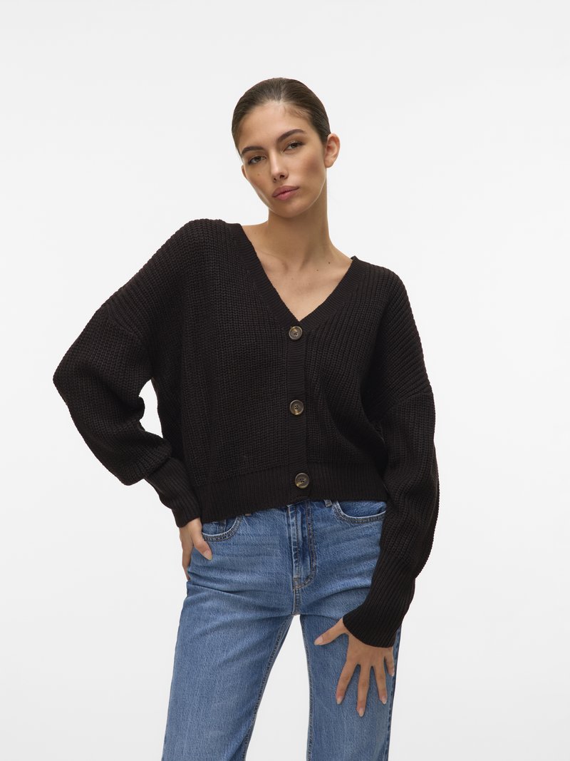Μαύρο πλεκτό cardigan με V-λαιμό, πέντε �κουμπιά και φαρδιές μανίκες, συνδυασμένο με ανοιχτό μπλε τζιν σε μπροστινή όψη.