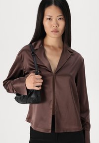Brown satin button-up shirt with a collar and long sleeves; paired with a small black textured handbag. Clean design and smooth texture.
