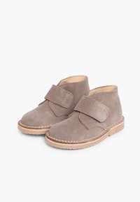 Stivali ankle in suede marrone con una fascia in velcro, punta rotonda e suola in gomma naturale, caratterizzati da semplice cucitura lungo i bordi.
