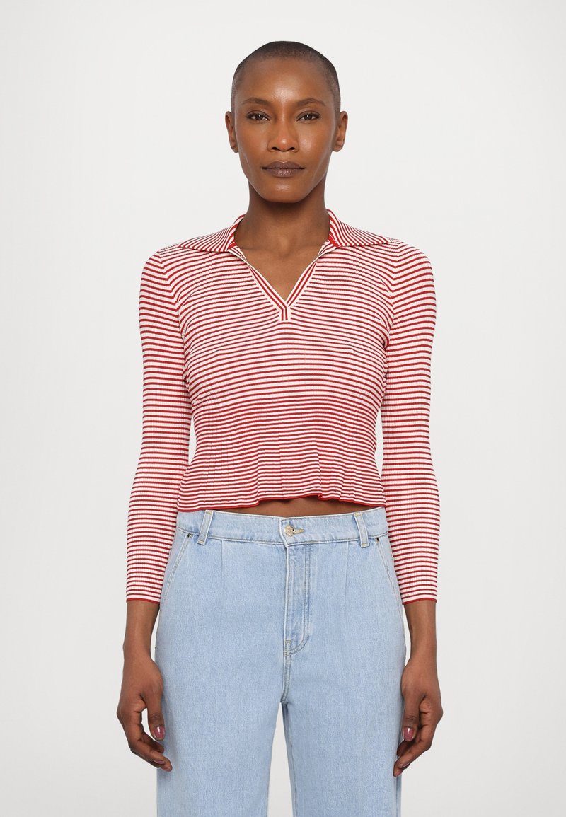 Polo rayé rouge et blanc à manches longues avec un col en V et une texture côtelée, associé à un jean taille haute bleu clair.