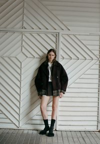 Maroon kaksirivinen villatakki valkoisen paidan päällä, yhdistettynä ruudullisiin hameisiin. Mustat ribbipolvisukat ja pörröiset mustat kengät. Geometrinen tausta.