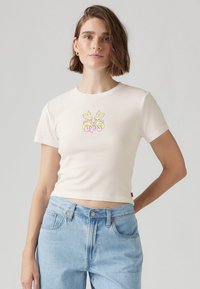T-shirt cropped de couleur crème en coton ; présente un graphique coloré de deux lapins roses sur le devant.