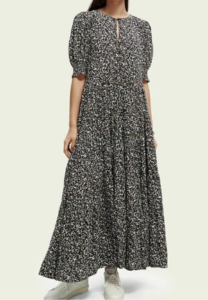 Maxikleid aus dunklem Stoff mit floralem Motiv, Puffärmeln, einem Schlüsselausschnitt und einer fließenden Silhouette, kombiniert mit weißen Turnschuhen.