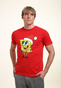Camiseta de algodón roja con un personaje de dibujos animados que lleva un gorro de Navidad. El personaje está sonriendo y destaca sobre el fondo vibrante.