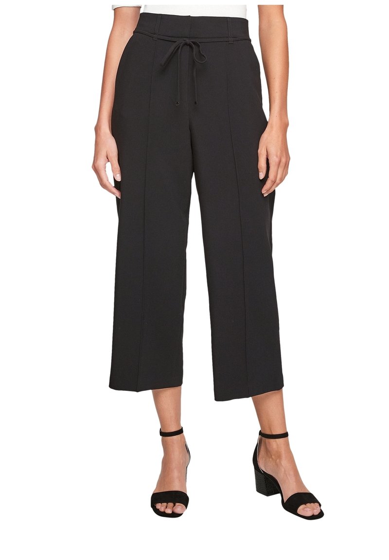 Pantalon large noir court taille haute avec couture frontale, taille nouée, porté avec des sandales à talons blocs noires à bride cheville.