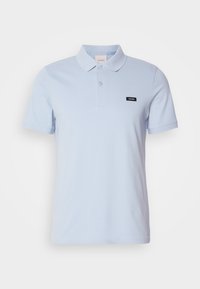 Polo bleu clair en coton, avec un col, deux boutons et un petit patch logo noir sur la poitrine gauche.