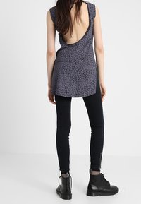Top ajustado sin mangas en púrpura oscuro con un sutil estampado de leopardo, con un escote profundo en la espalda. Combinado con jeans negros ajustados y botas.