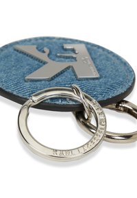 Μπρελόκ από τζιν με κυκλικό σχήμα, ασημένια λεπτομέρεια λογότυπου και μεταλλικό κρίκο. Υφασμάτινη υφή με μαύρη λαστιχένια άκρη και χαραγμένα εξαρτήματα.