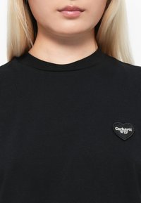 Black cotton t-shirt with a round neck, featuring a heart-shaped black patch with white text "Carhartt WIP" on the left chest area.