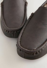 Bruine leren slippers met een platte ontwerp, dikke stiksels langs de randen en een zachte, gestructureerde afwerking voor comfort.