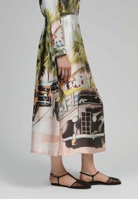 Robe midi en soie avec un imprimé de voiture vintage coloré, des palmiers et un fond rose pâle. Associée à des sandales noires à brides.