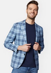 Jasnoniebieska marynarka w kratę z ciemniejszymi niebieskimi akcentami, zapinana na jeden guzik, z klapami w kształcie notcha, noszona na granatowej koszulce i dżinsowych spodniach.