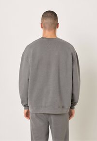 Hall grey oversize-sviiter ribatud mansettide ja allääriga, valmistatud pehmest, tekstuuriga kangast, klassikalise ümmarguse kaeluse ja langetatud õlgadega.