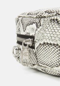 Černobílá kabelka s hadím vzorem, se stříbrnými detaily, zipovým uzávěrem a kulatým upevňovacím kroužkem. Texturovaný povrch.