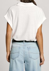 Vit kortärmad skjorta med en vikbar krage. Kombinerad med ljusblå högmidjade jeans med bakfickor och ett svart bälte.