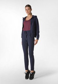 Marinträningsdräkt med zip-up hoodie och byxor med dragsko, i kombination med svarta träningssneakers. Tyget verkar slätt och ventilerande.