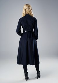 Granatowa sukienka koszulowa z długimi rękawami, elastycznym paskiem w talii i rozkloszowanym dołem. Czarny pasek podkreśla talię. Gładka tekstura, bez widocznych wzorów.