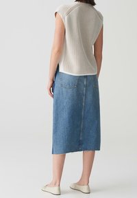 Haut en maille à manches courtes couleur crème avec côtes verticales ; jupe en jean taille haute bleu avec deux poches arrière et ourlet effiloché.