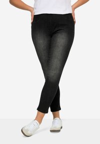 Vaqueros de mezclilla negra con un ajuste slim, cintura de altura media y un desvanecimiento sutil. Combinados con zapatillas blancas con acentos grises.