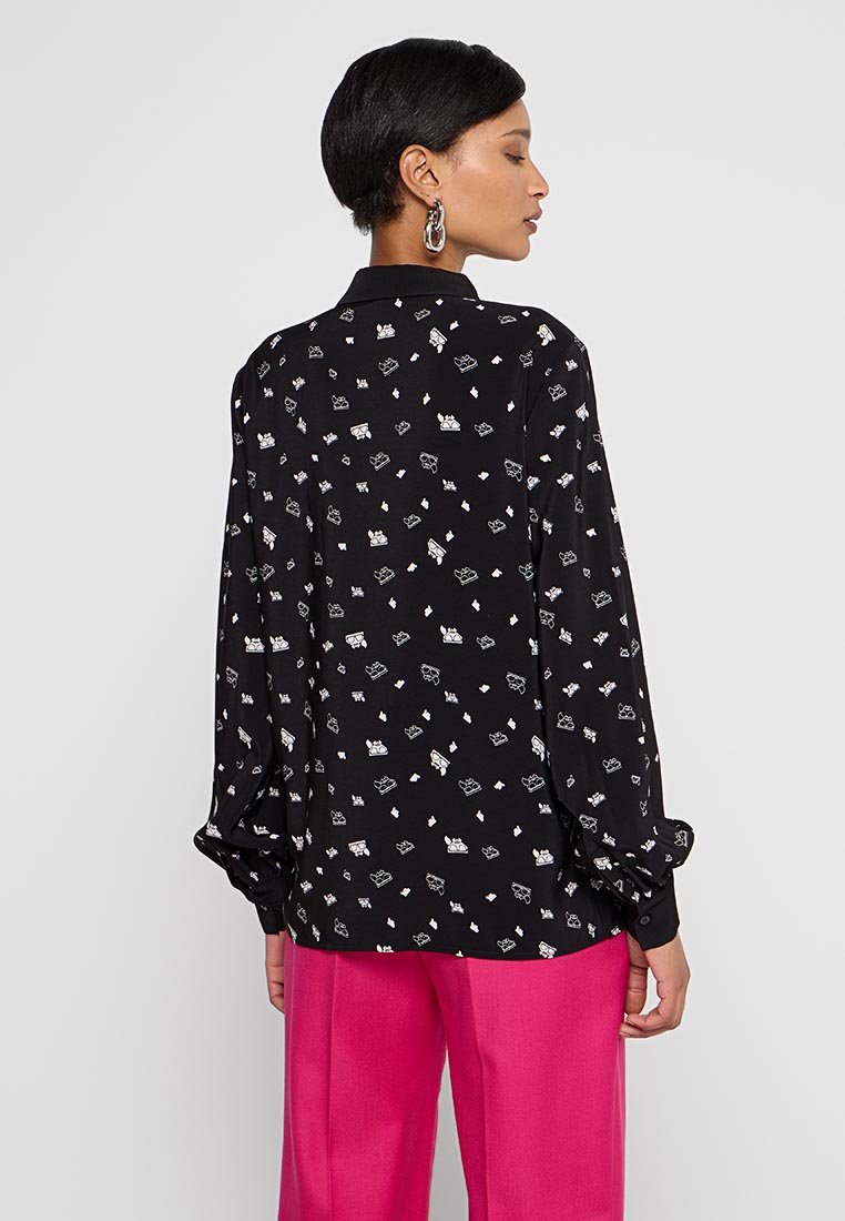 Camisa negra de manga larga con un patrón gráfico blanco repetido, con un corte relajado y puños abotonados. Combinada con pantalones de pierna ancha rosas.