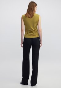 Top senza maniche verde oliva con dettaglio arricciato sul retro, abbinato a pantaloni neri sartoriali, mostrato da dietro. Tessuto di trama liscia.